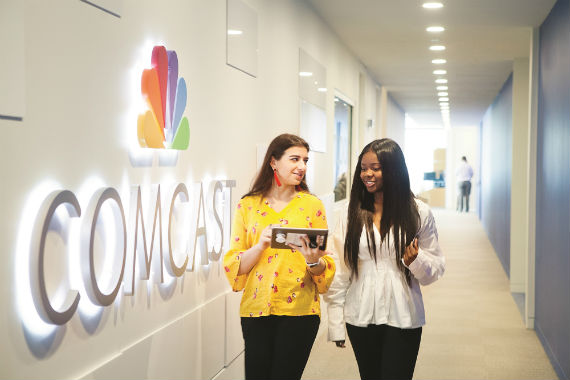 Two females walking down a hall with the comcast logo on one wall 